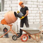 a man in a hard hat holding a bucket and cement mixer