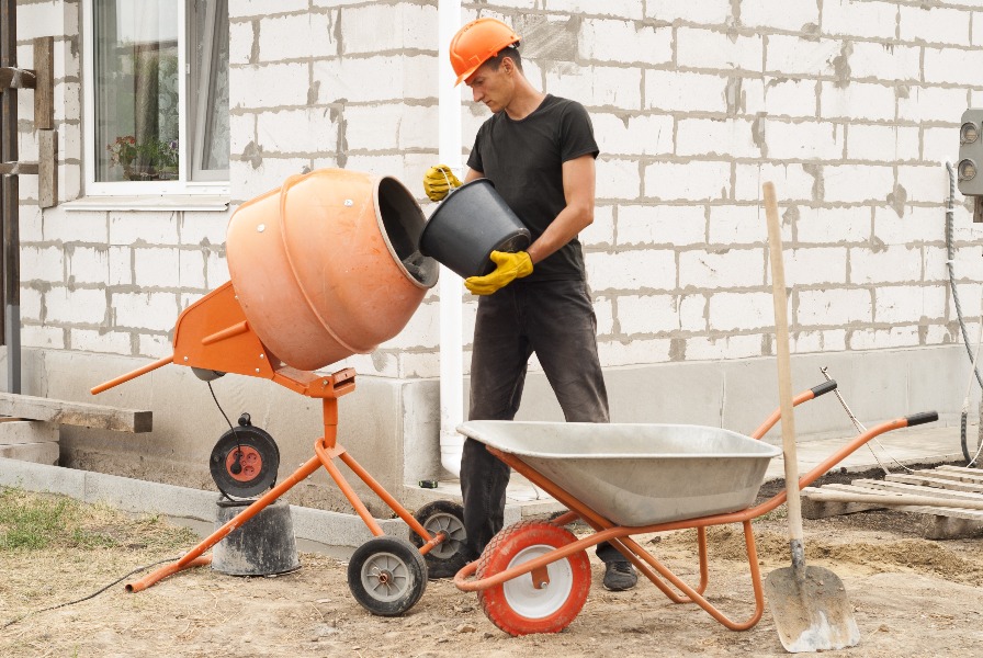 a man in a hard hat holding a bucket and cement mixer